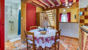 Zona de menjador amb taula rodona, cadires, una porta vermella, sostre de fusta i una finestra amb cortines vermelles.