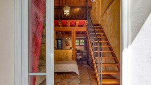Unes escales de fusta que condueixen a un dormitori tipus altell amb un llit i una cadira.