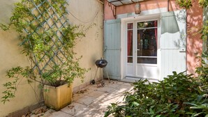 Un pati amb una planta en test, una barbacoa i una porta amb finestral.
