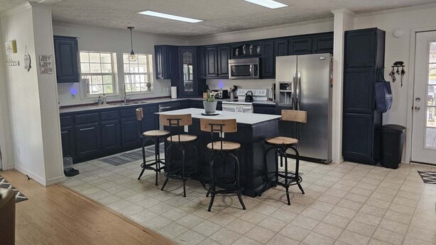 Een moderne keuken met donkerblauwe kastjes, een roestvrijstalen koelkast, een magnetron en een centraal eiland met barstoelen.