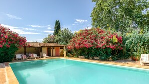 Una piscina con sillones de descanso, un edificio con techo de tejas y abundante vegetación.