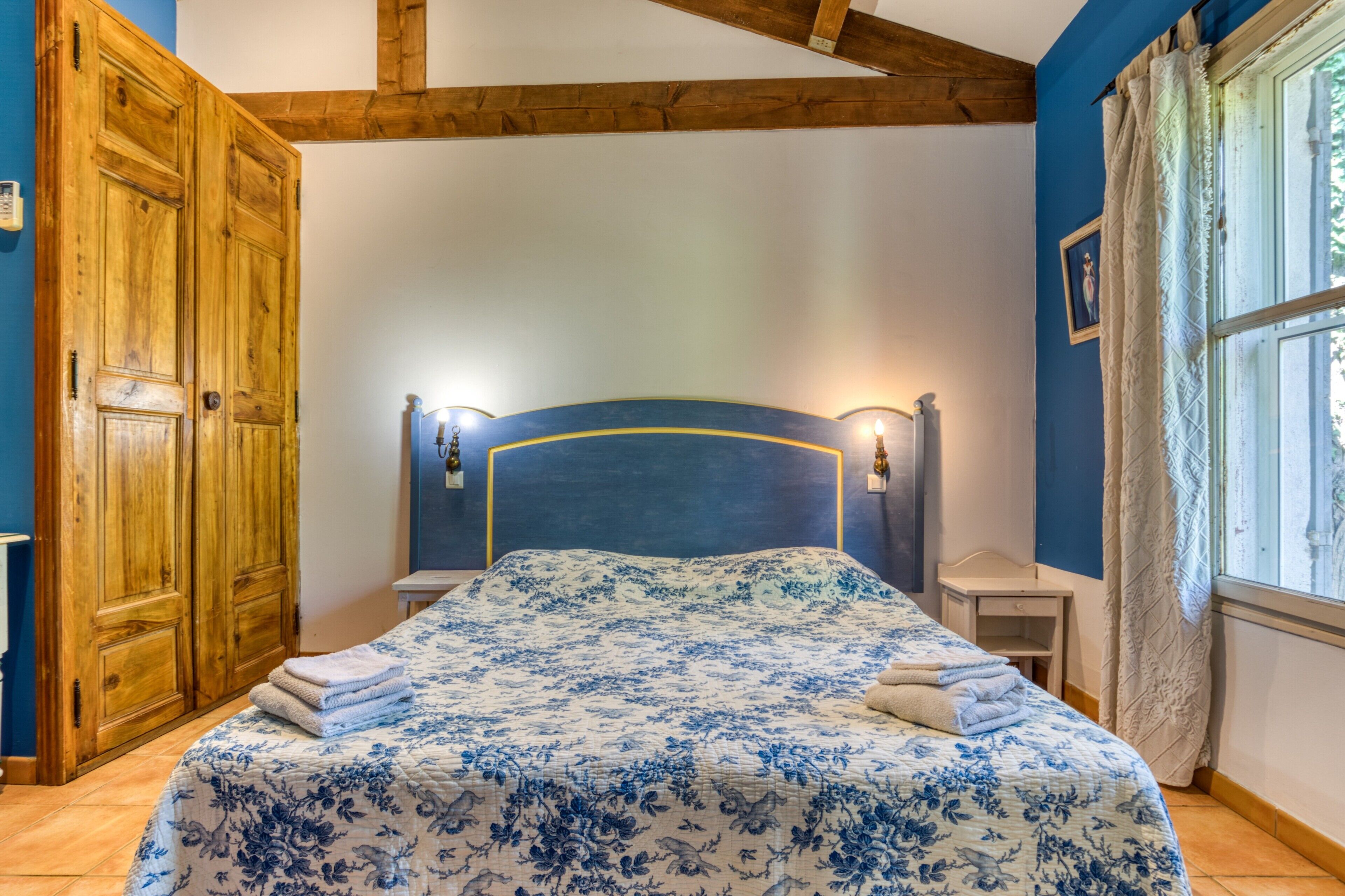 Ein Schlafzimmer mit einem Bett, einem Holzschrank, Nachttischen und einem Fenster mit Vorhängen.