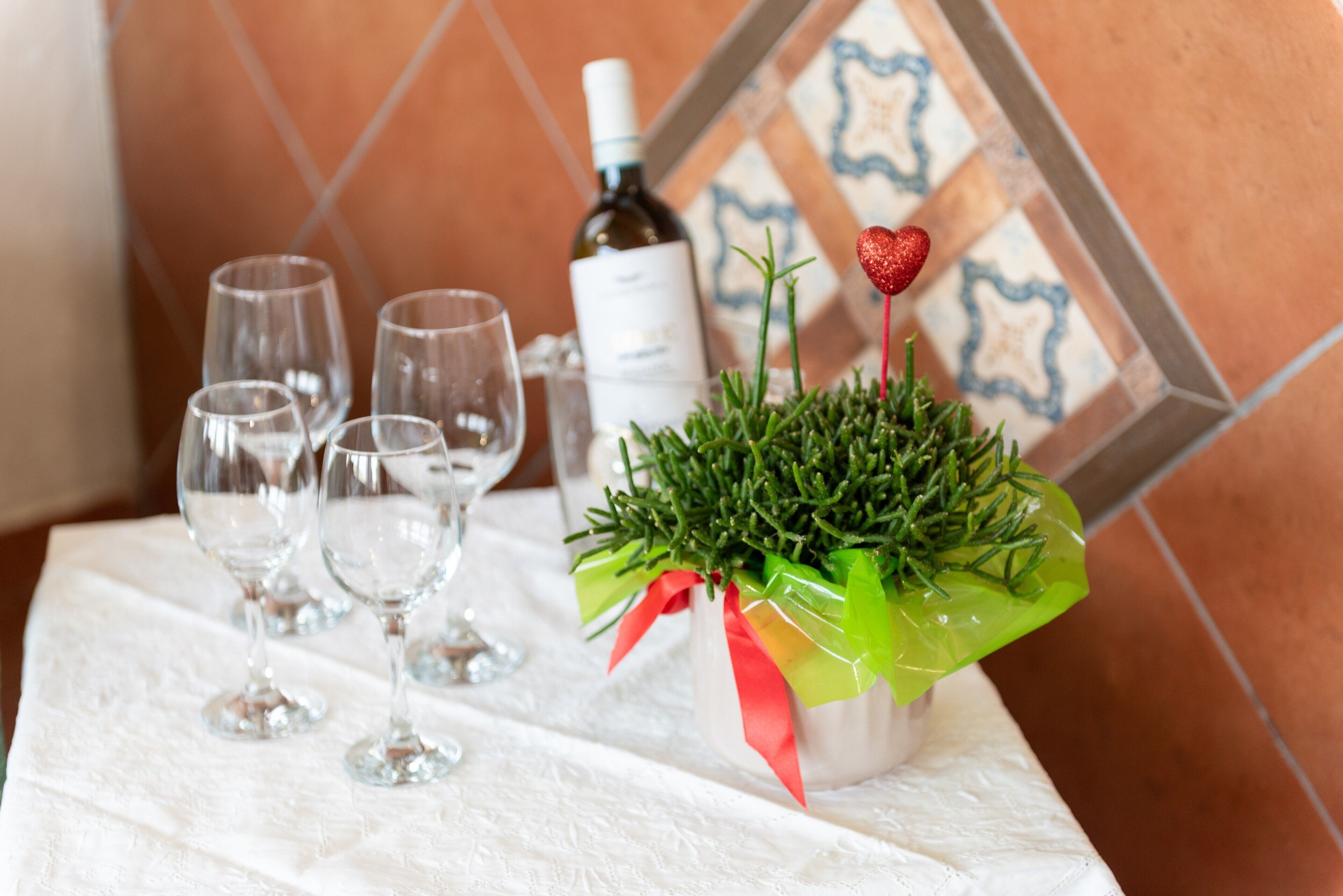 Une table avec des verres à vin, une bouteille de vin et une petite plante en pot décorée d’un cœur rouge.