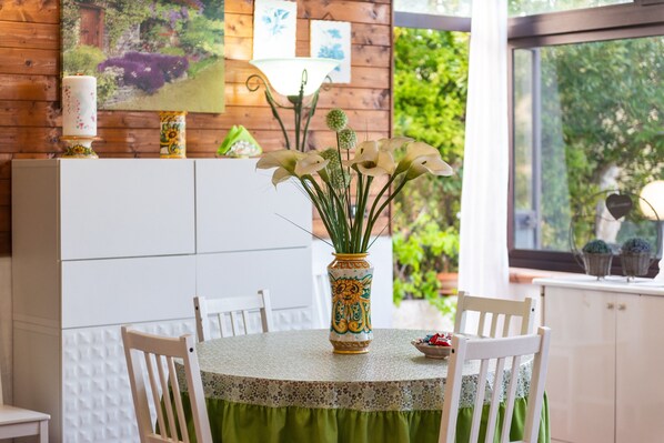 A dining area with a round table, chairs, a vase with flowers, and a wall with framed pictures.