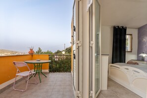 A balcony with a table and chairs, a bed with a nightstand, and a view of the city.