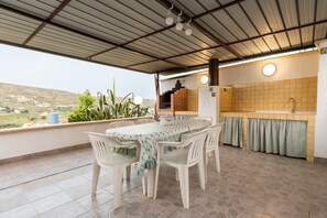 A covered patio with a table and chairs, a kitchen area with a sink and tiled backsplash, and a view of the countryside.
