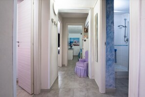 A hallway leading to a bathroom with a shower, a purple chair, and a painting on the wall.