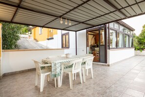 A covered patio area with a table and chairs, a view of the house, and a door leading to the interior.