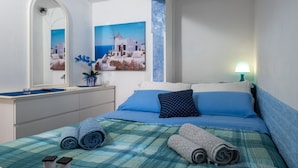 A hotel room with a bed, a mirror, a painting of a coastal scene, a lamp, and towels. - Holiday Home 'Casa Montereale' with Sea View, Private Terrace and Wi-Fi (Realmonte)