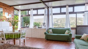 A kitchen with a dining table, chairs, a green sofa, and a view of the countryside through large windows. - Holiday Home 'Casa Montereale' with Sea View, Private Terrace and Wi-Fi (Realmonte)