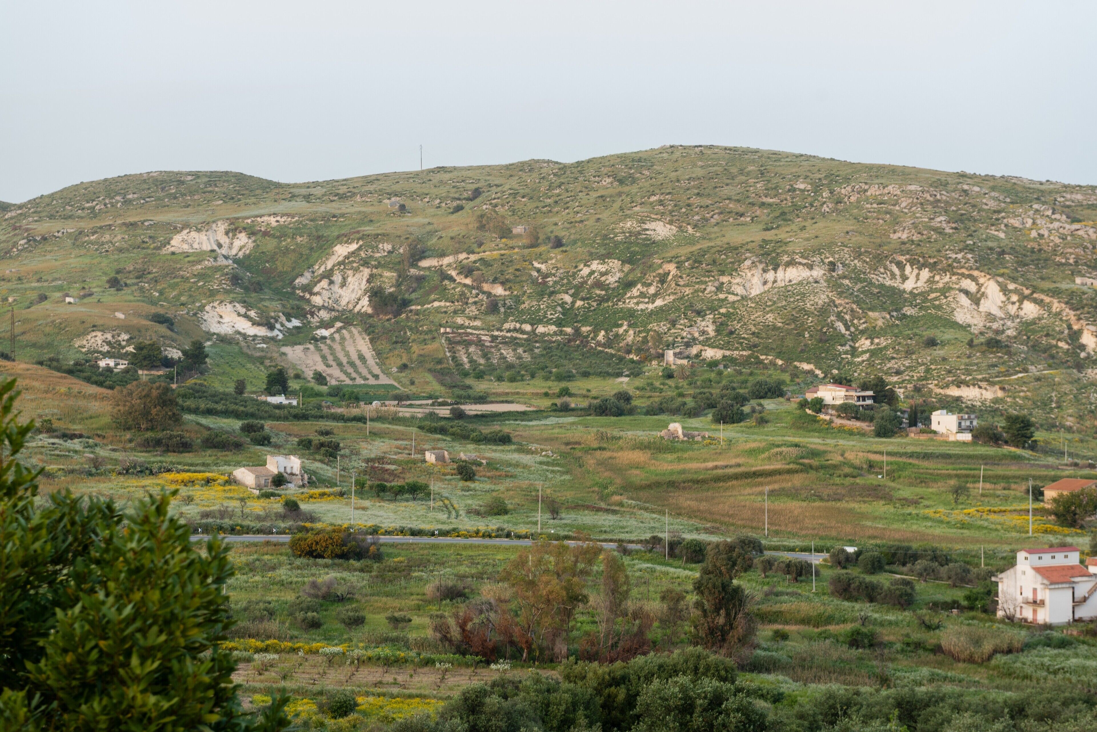 A rural landscape with rolling hills, scattered houses, and a road.