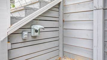 Un angolo di un edificio con rivestimento in legno bianco, una scala in metallo e un quadro elettrico con una presa.