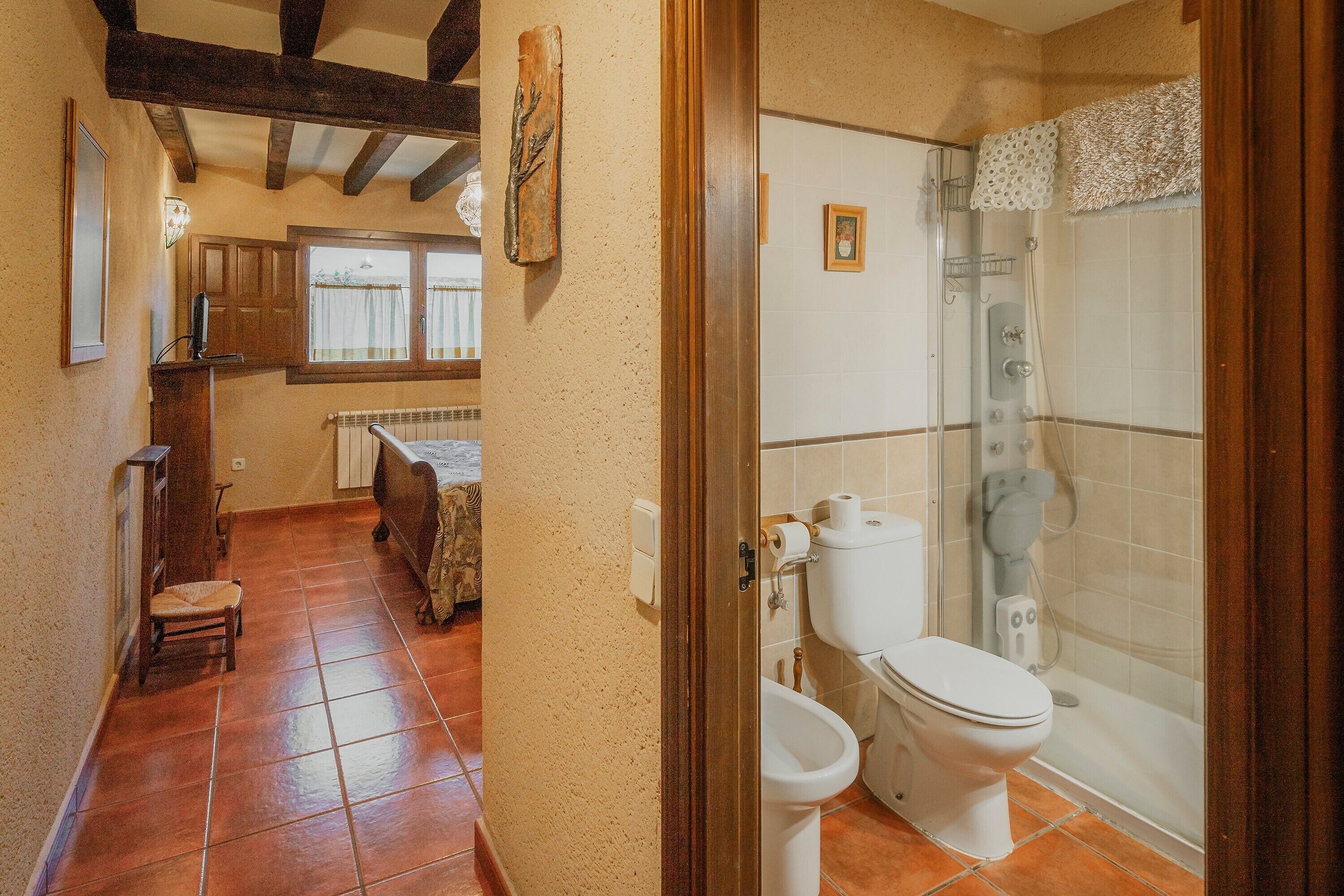 Een badkamer met toilet, bidet en douche. Er is een raam met gordijnen en een radiator.