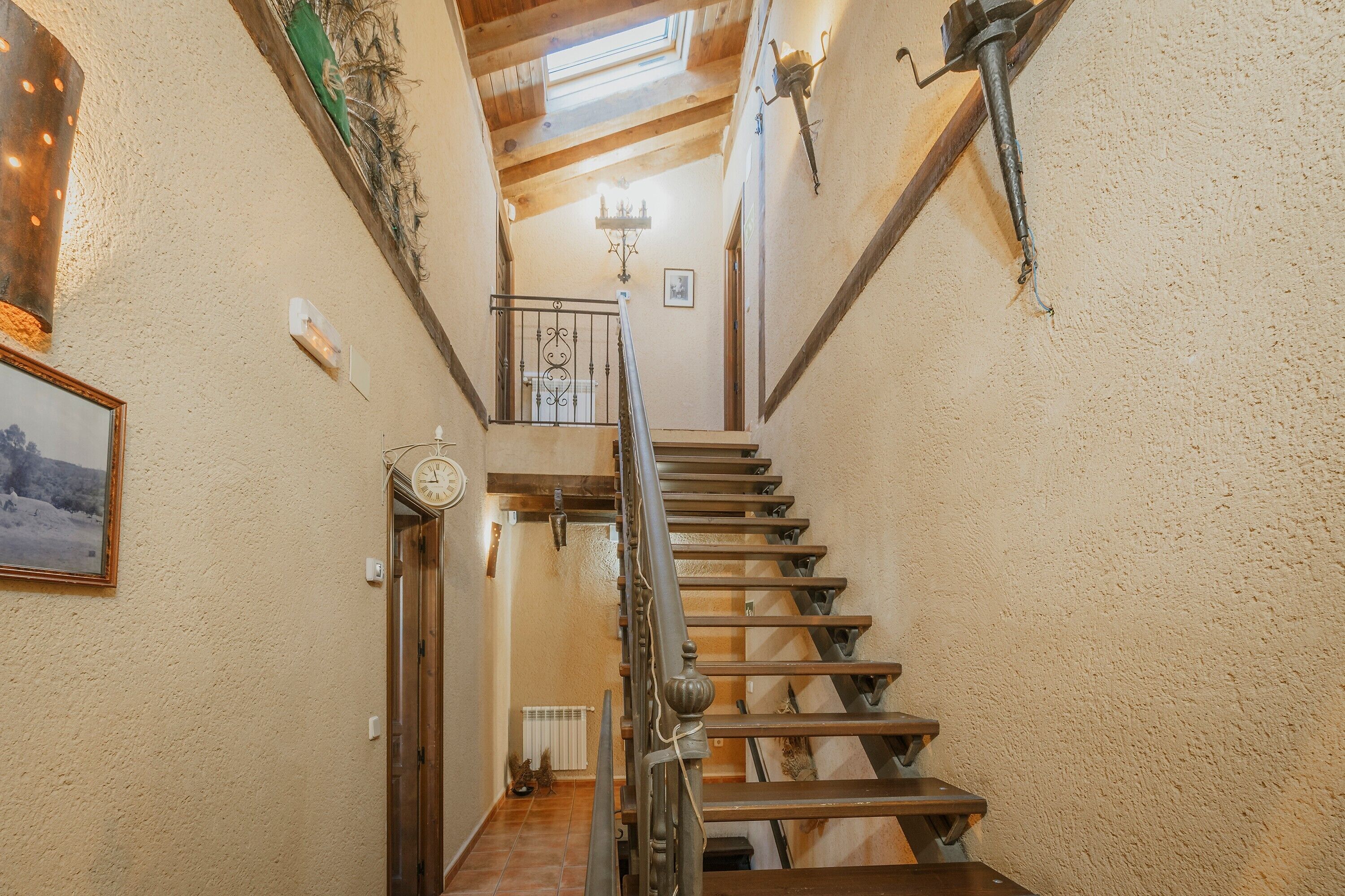 A staircase with wooden steps and metal railings, leading to a landing with a chandelier and a framed picture on the wall.
