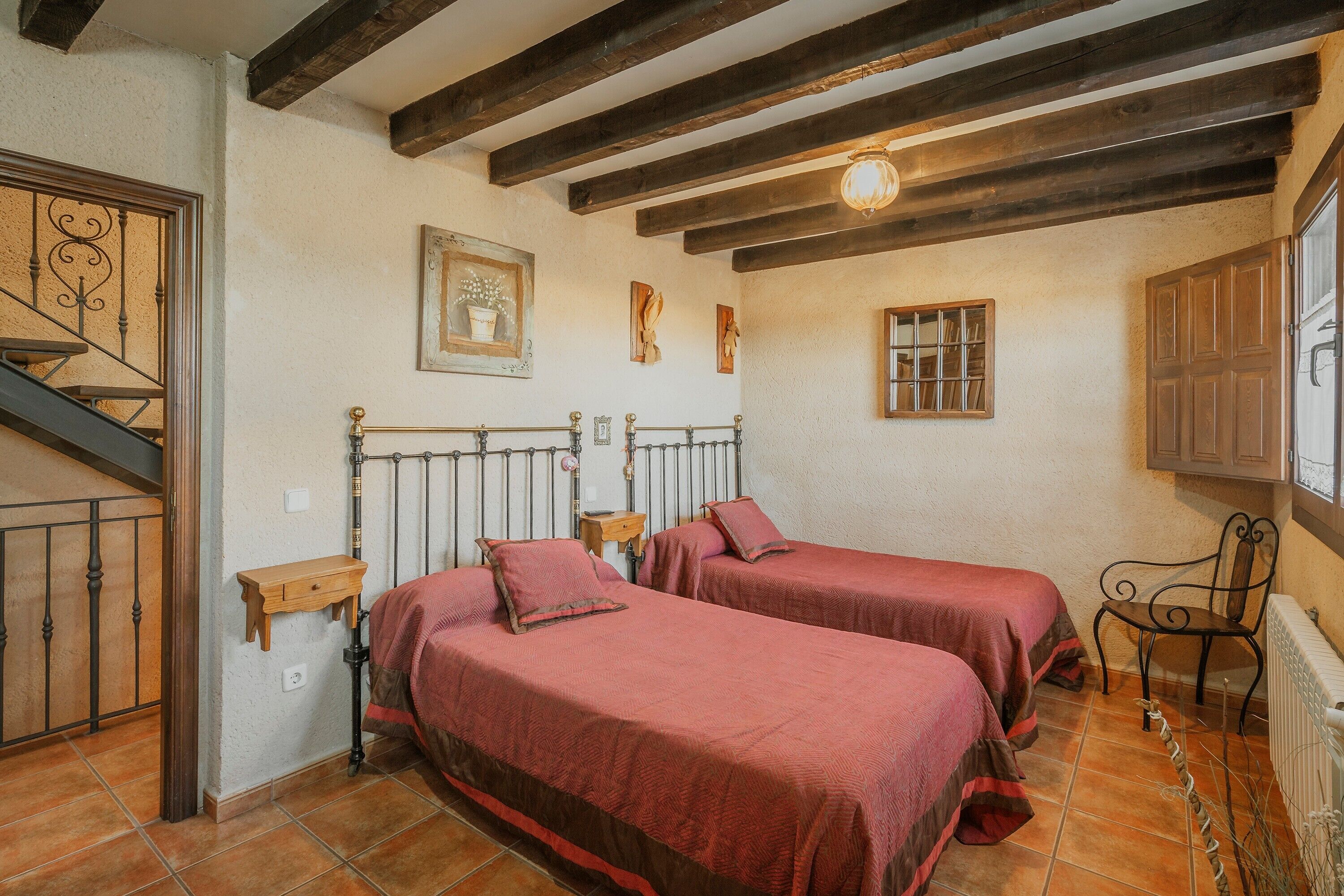 Una habitación con dos camas, vigas de madera en el techo, una mesita y una silla.
