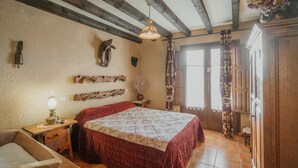 Ein rustikales Schlafzimmer mit einem hölzernen Bett, einem Nachttisch aus Holz, einer Lampe, einem Holzstuhl, einem Schrank aus Holz und einem Fenster mit Vorhängen.