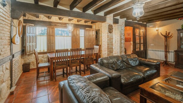 Ein gemütliches Wohnzimmer mit Ledersofa, Esstisch aus Holz und Stühlen, Kamin und Steinwand.