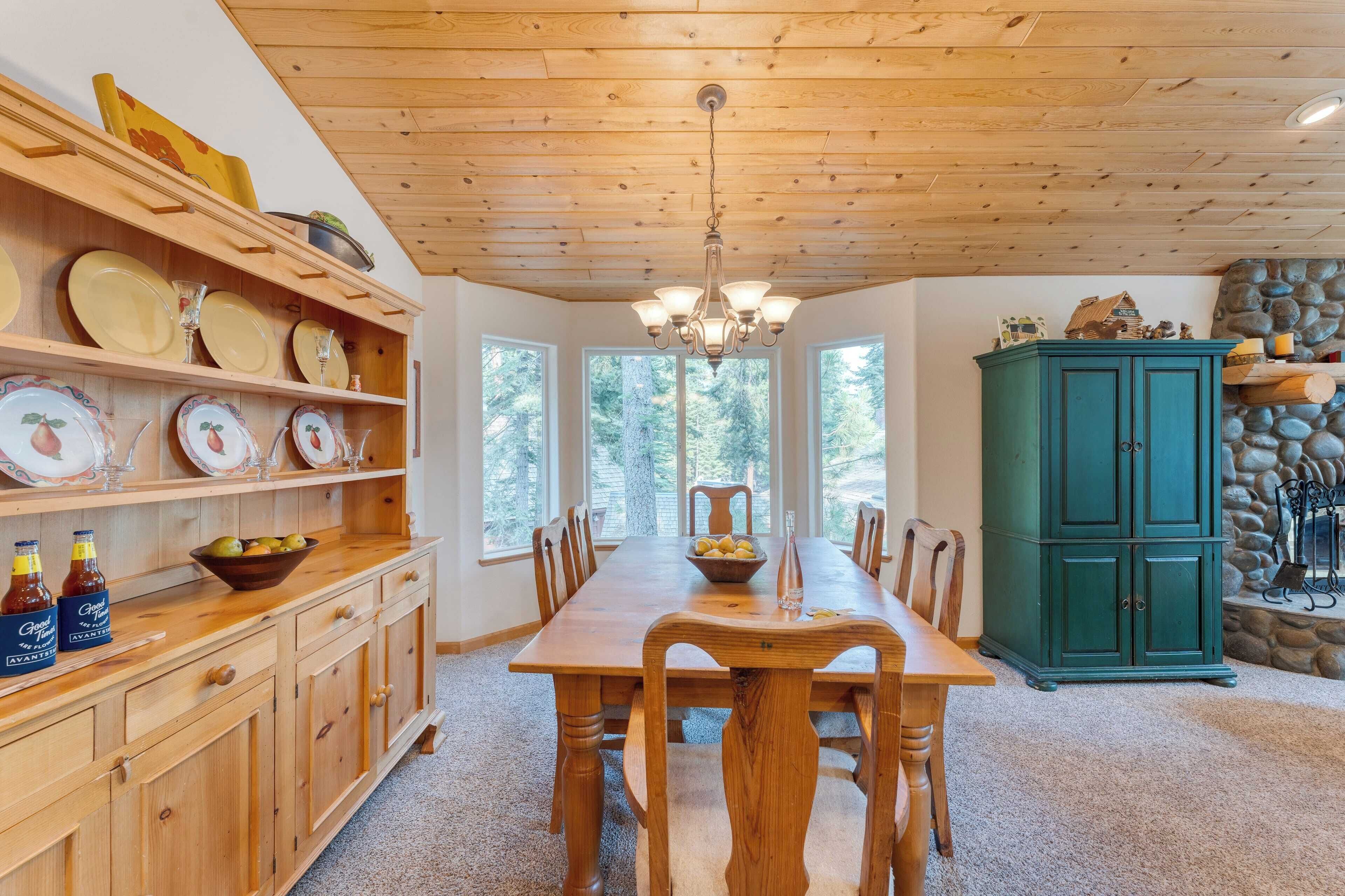 A wooden dining room with a large table, chairs, and a chandelier. There are shelves with plates and bowls, and a green cabinet.