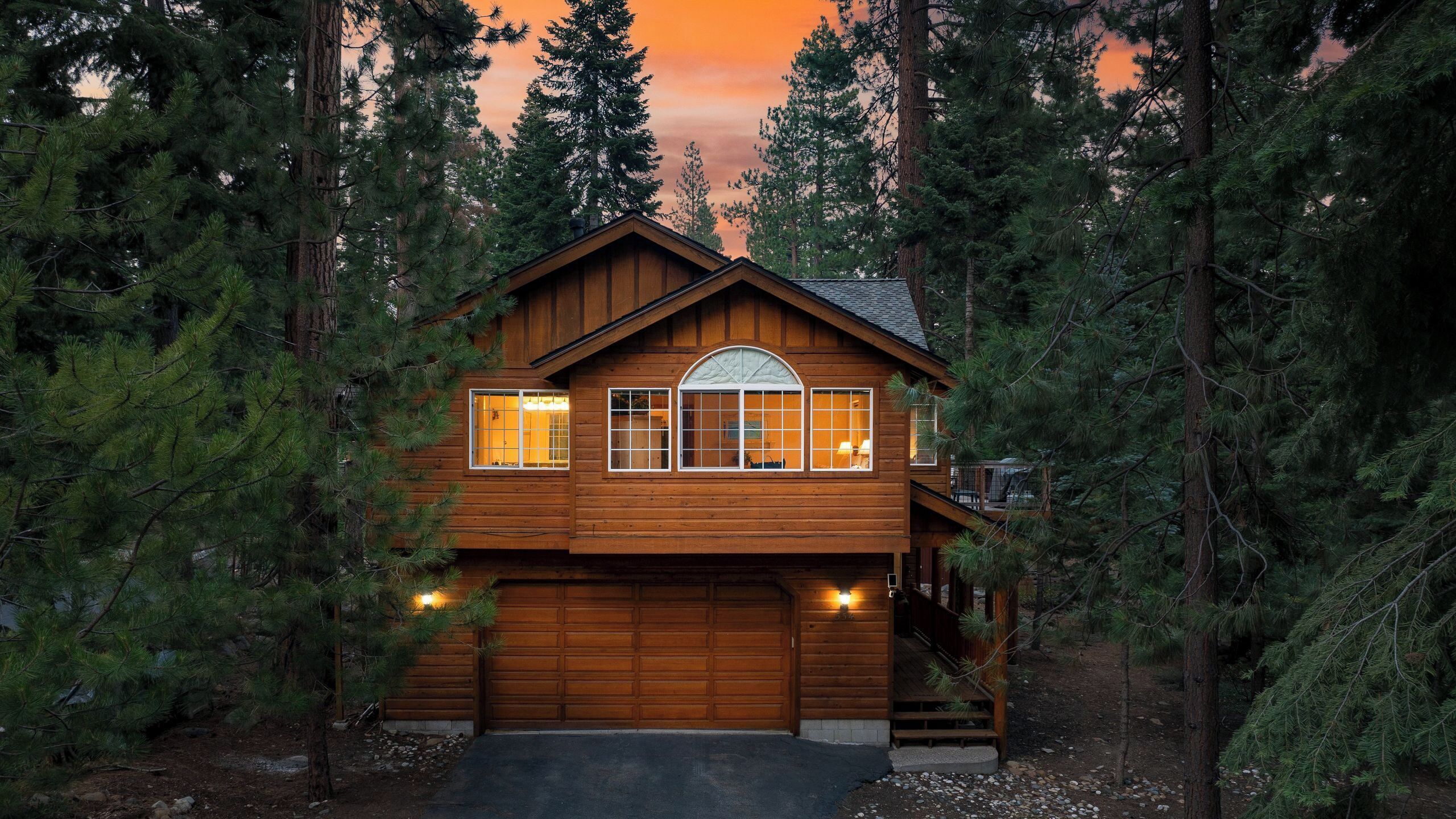 A two-story log cabin with a garage, surrounded by tall pine trees.