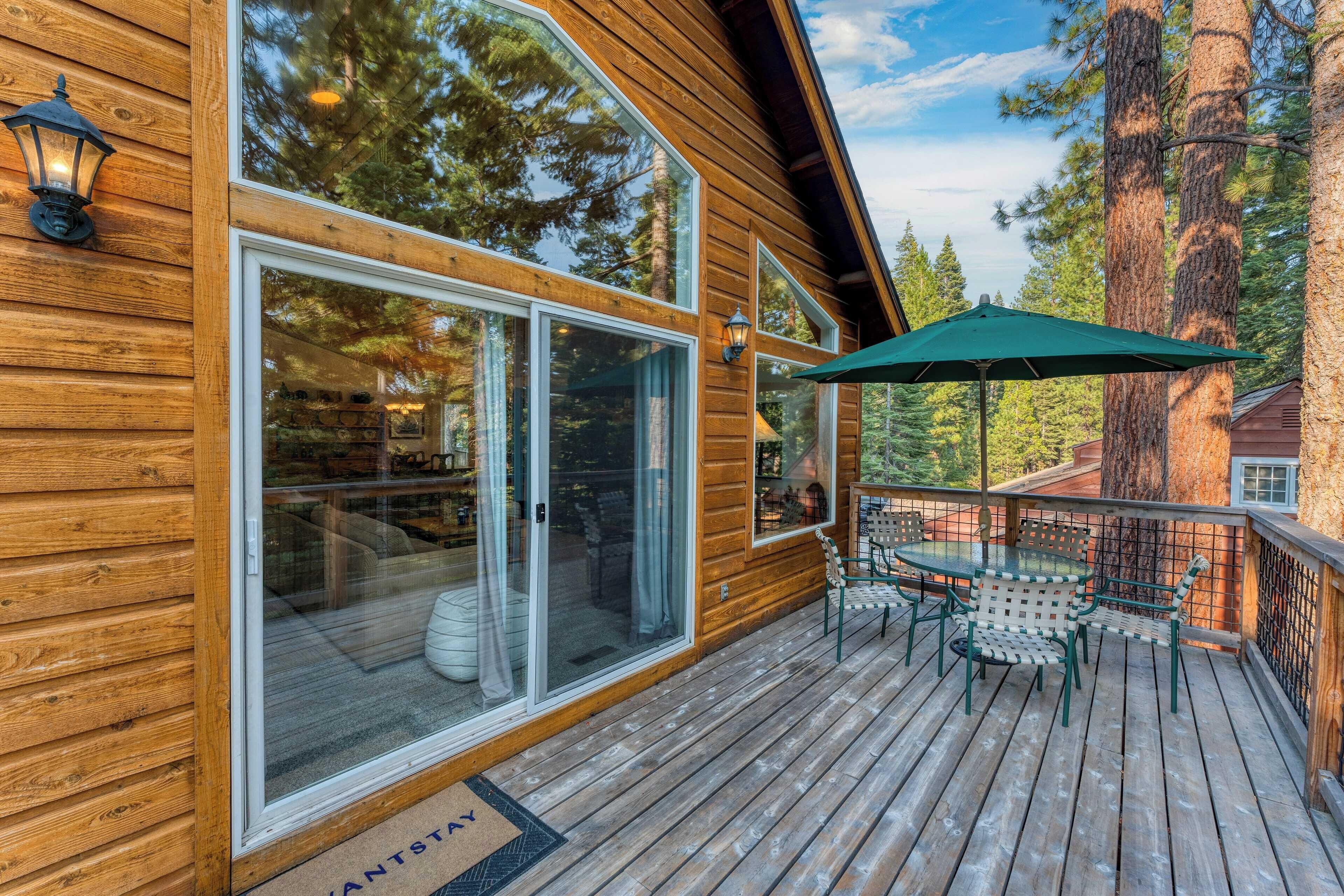 A wooden cabin with large windows, a deck with outdoor furniture, and a view of tall trees.