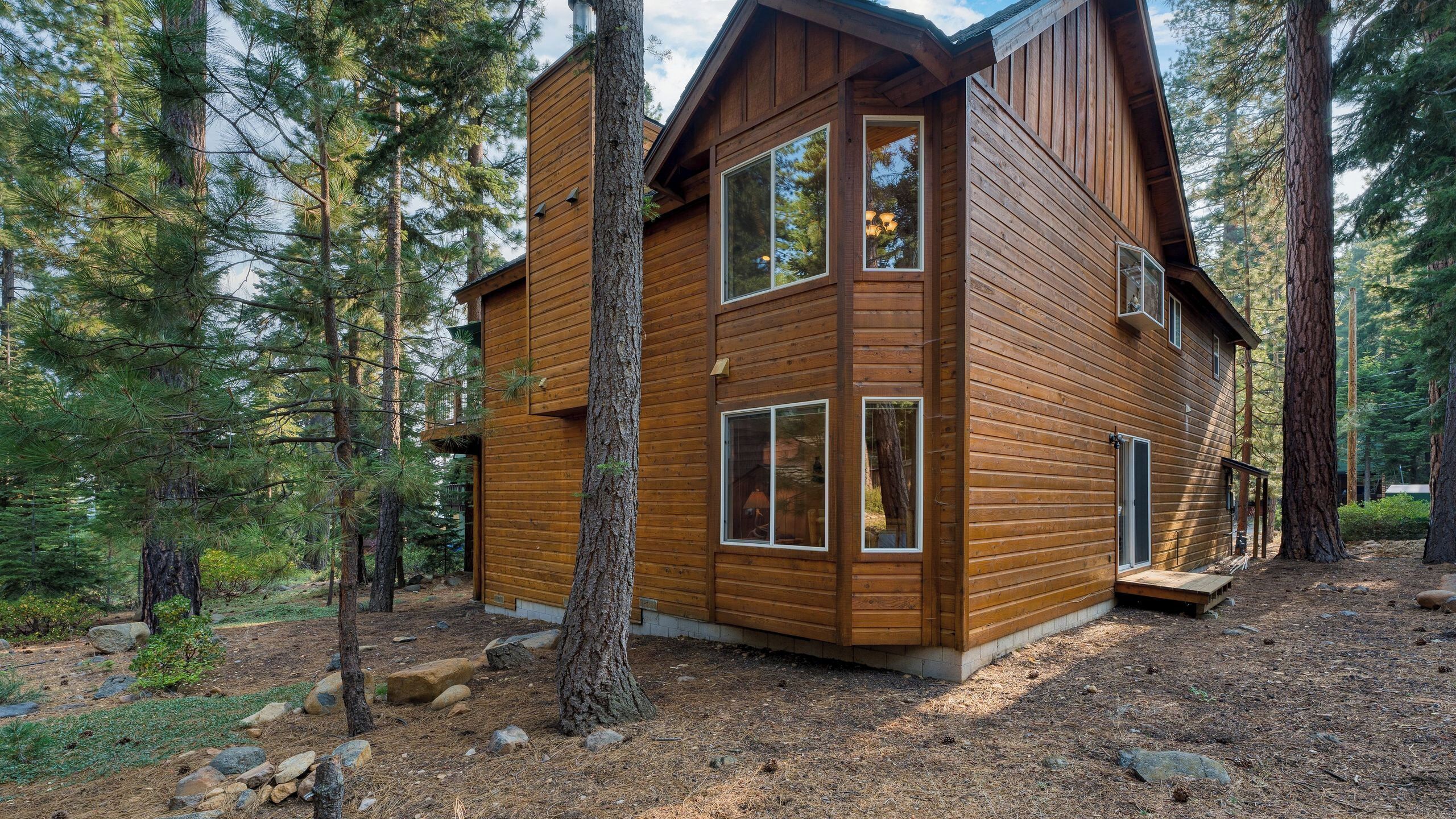 A two-story wooden cabin surrounded by tall pine trees.
