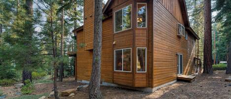 A two-story wooden cabin surrounded by tall pine trees.
