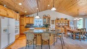 A kitchen with wooden cabinets, a central island with chairs, and a dining area with a table and chairs. - Tahoe Vista by Avantstay Central Location + Patio (Tahoe Vista)