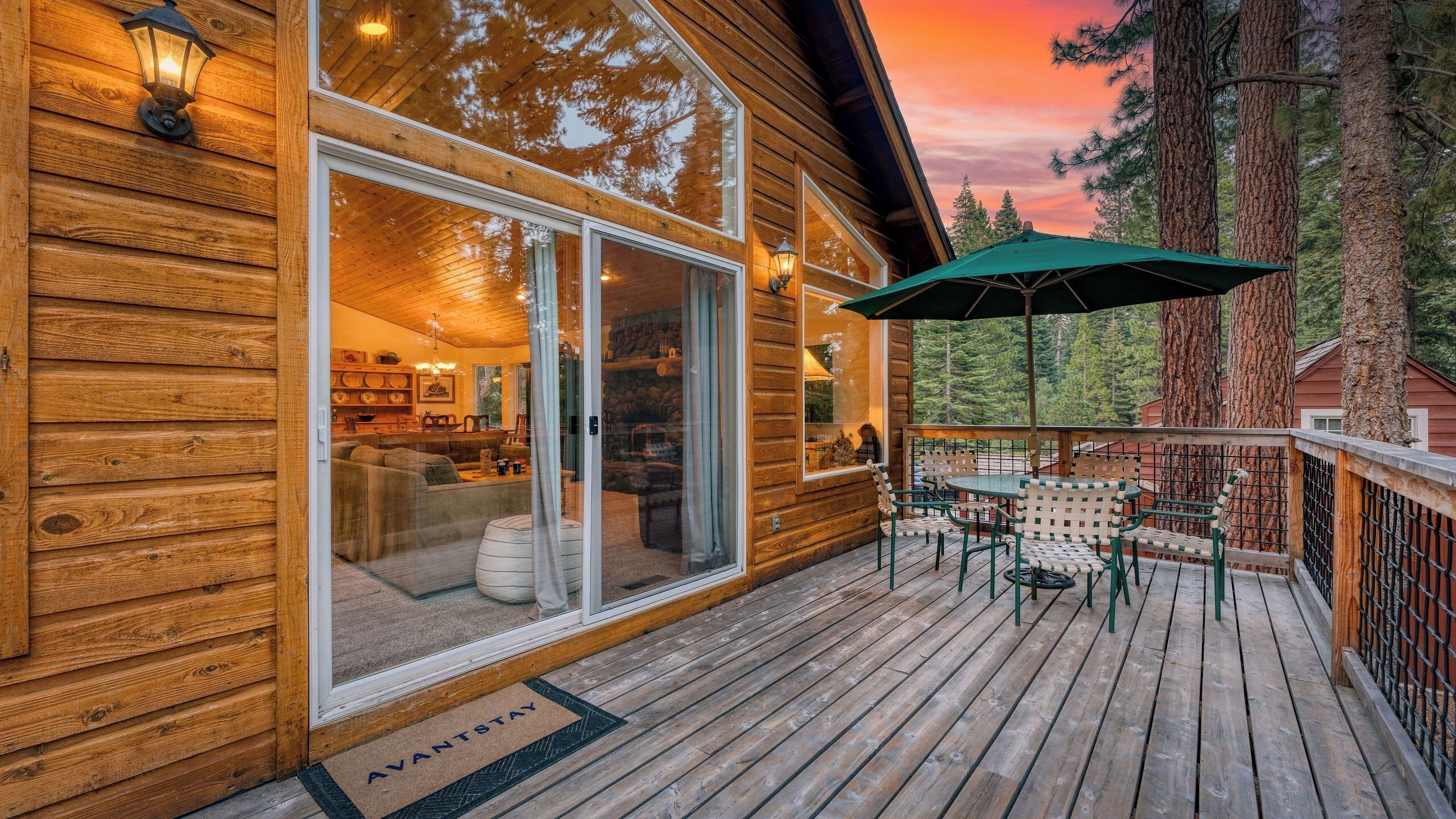 A wooden cabin with a deck, large windows, and a green umbrella.