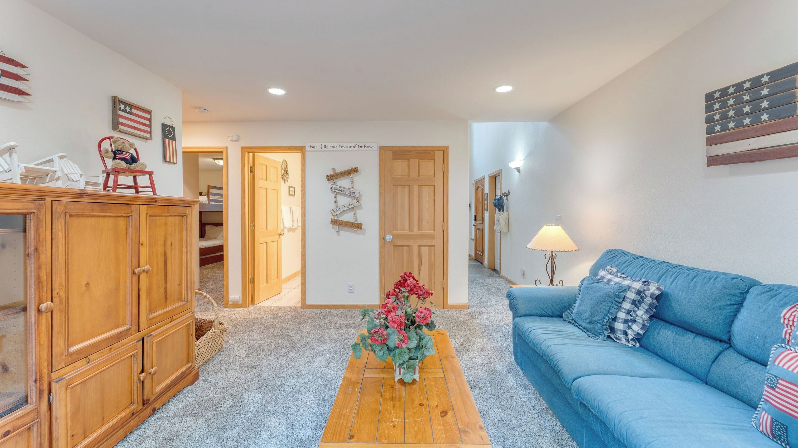 A room with a blue couch, wooden cabinets, a wooden table with flowers, and a door with signs.