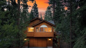 A two-story log cabin with a garage, surrounded by tall pine trees, at dusk. - Tahoe Vista by Avantstay Central Location + Patio (Tahoe Vista)
