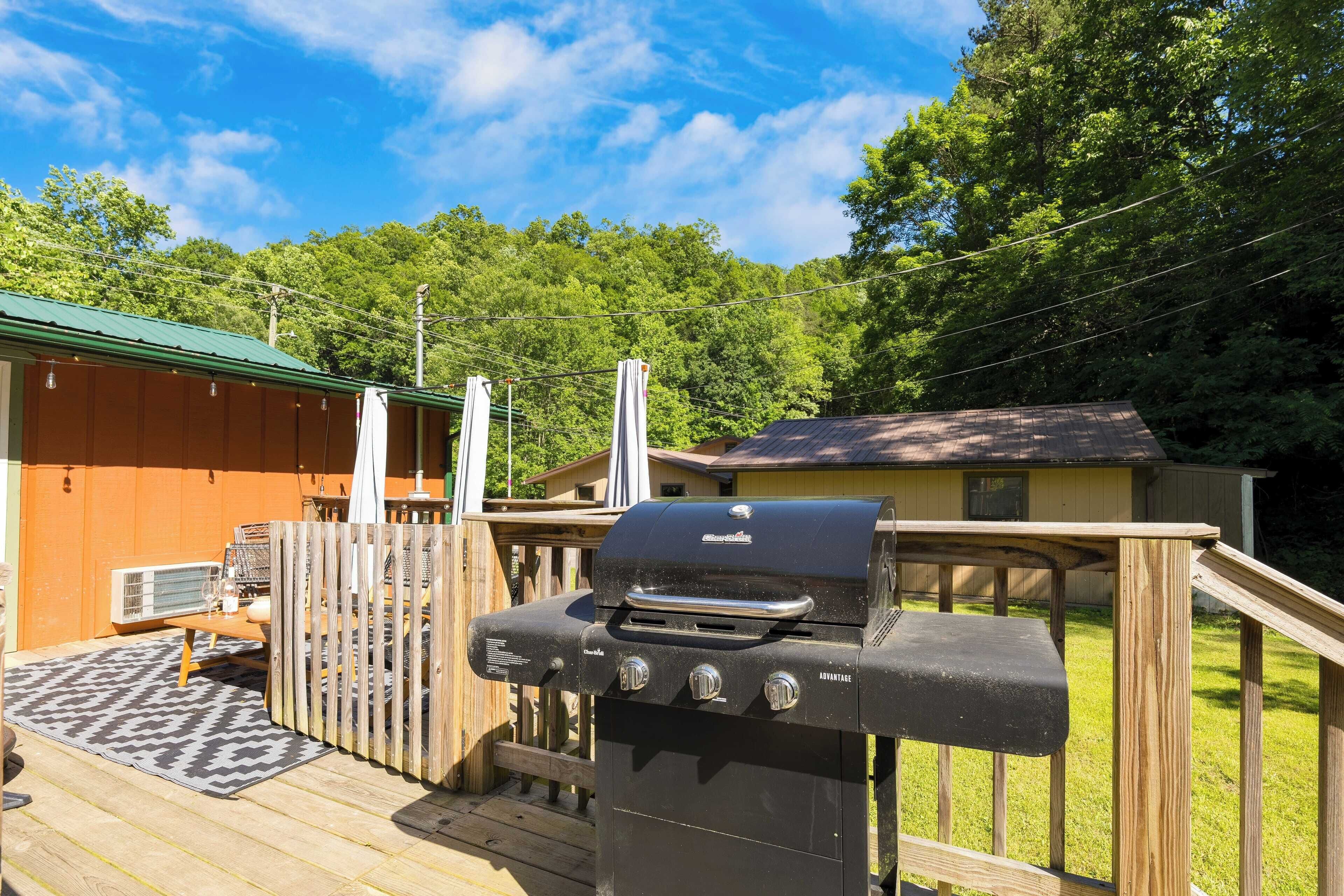 A barbecue grill on a wooden deck with a view of a house and trees in the background.