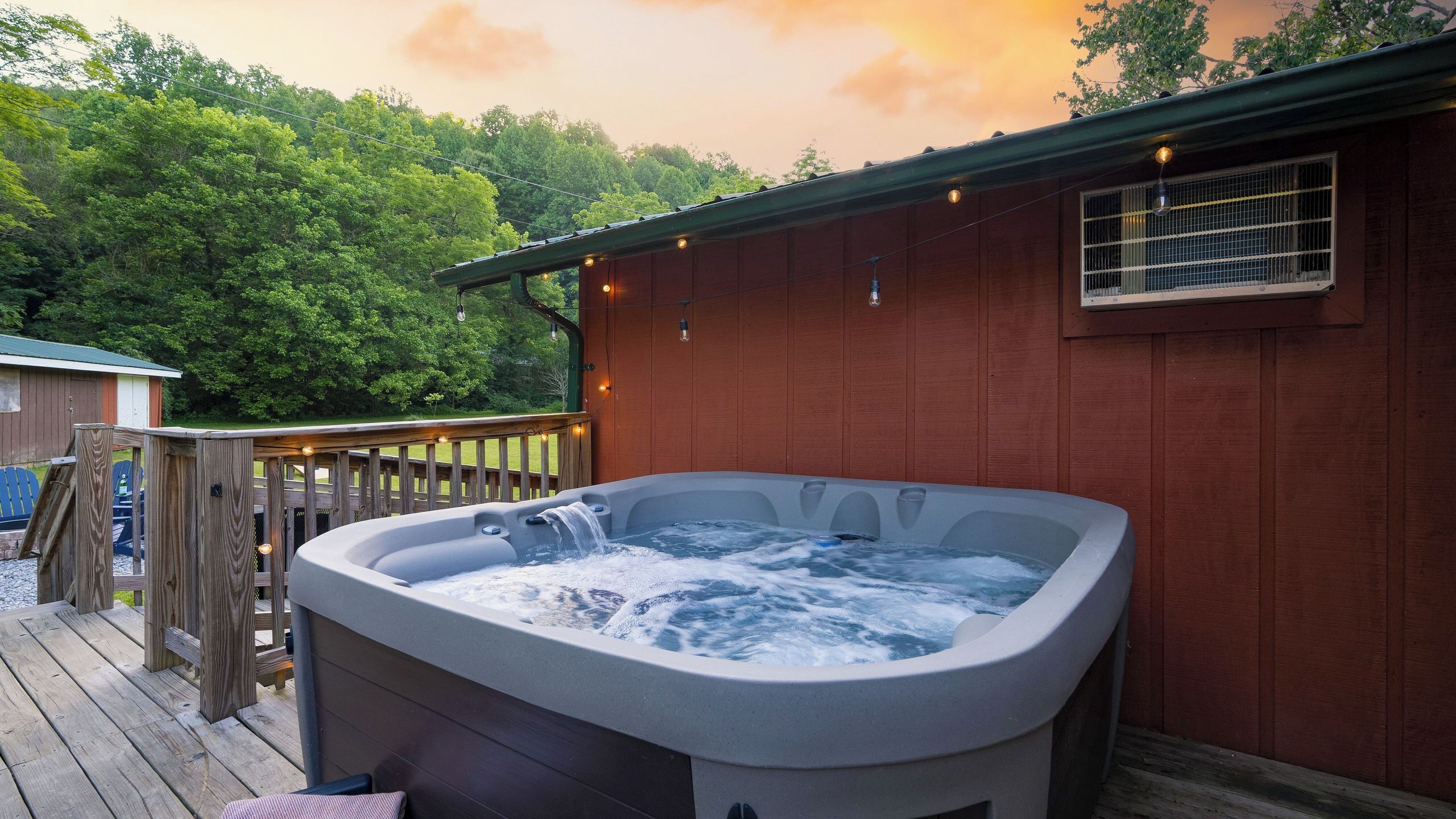 A hot tub on a wooden deck with a wooden fence and a building in the background.