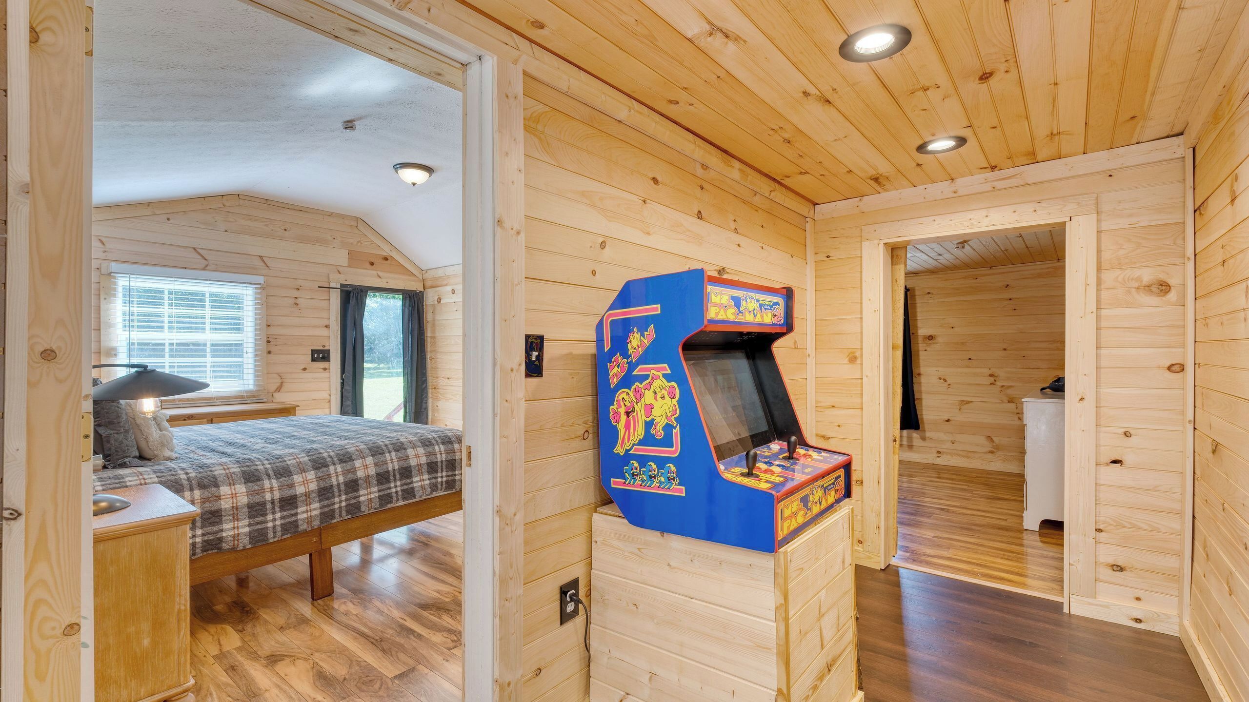 A wooden cabin with a bed, a desk, a lamp, and a Pac-Man arcade game.