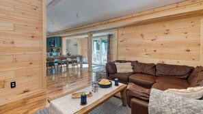 A wooden interior with a sofa, coffee table, and a dining area with chairs and a table.