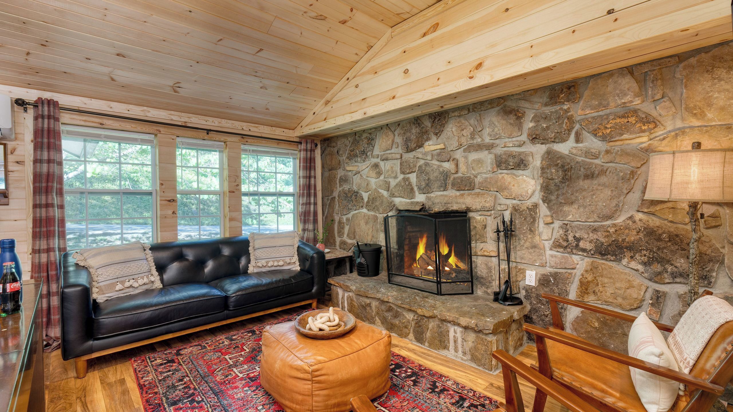A cozy room with a stone fireplace, a black leather sofa, a wooden coffee table, and a stone wall.