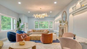 A modern living room with a fireplace, large windows, and a chandelier.