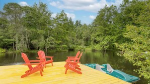 A wooden dock with two red Adirondack chairs and a green rowboat.