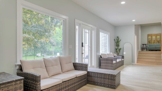 A spacious living area with a large window, wicker furniture, and a staircase leading to an upper level.