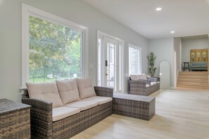A spacious living area with a large window, wicker furniture, and a staircase leading to an upper level. - Game Farm Villa by Avantstay 10bdr, Private Pond, Spa, Pool Family-friendly (Palenville)