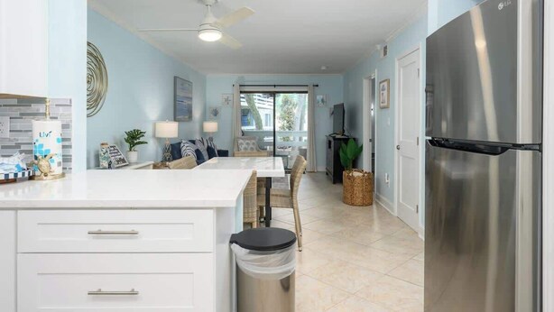 A modern kitchen with a stainless steel refrigerator, white cabinetry, and a dining area with a table and chairs.