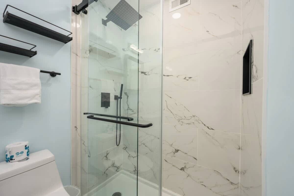 The shower is enclosed in glass and finished with white marble-patterned tiles.