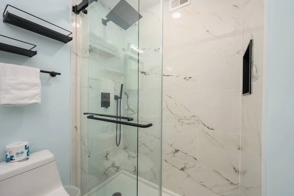 The shower is enclosed in glass and finished with white marble-patterned tiles.