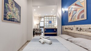 Hotellihuone, jossa on sänky, kaksi tyynyä, sängynpääty, yöpöytä, työpöytä, tuoli ja ikkuna, jossa on verhot.