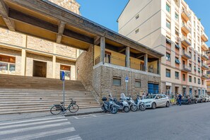 A building with a stone facade, a staircase, and a row of parked scooters and cars.