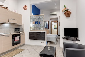 Cocina moderna con microondas, horno y separador de vidrio. Hay un televisor de pantalla plana, un sofá y una cama con una pared de acento azul.