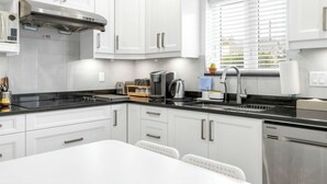 Una cocina moderna con armarios blancos, encimera negra, electrodomésticos de acero inoxidable y una ventana con persianas.