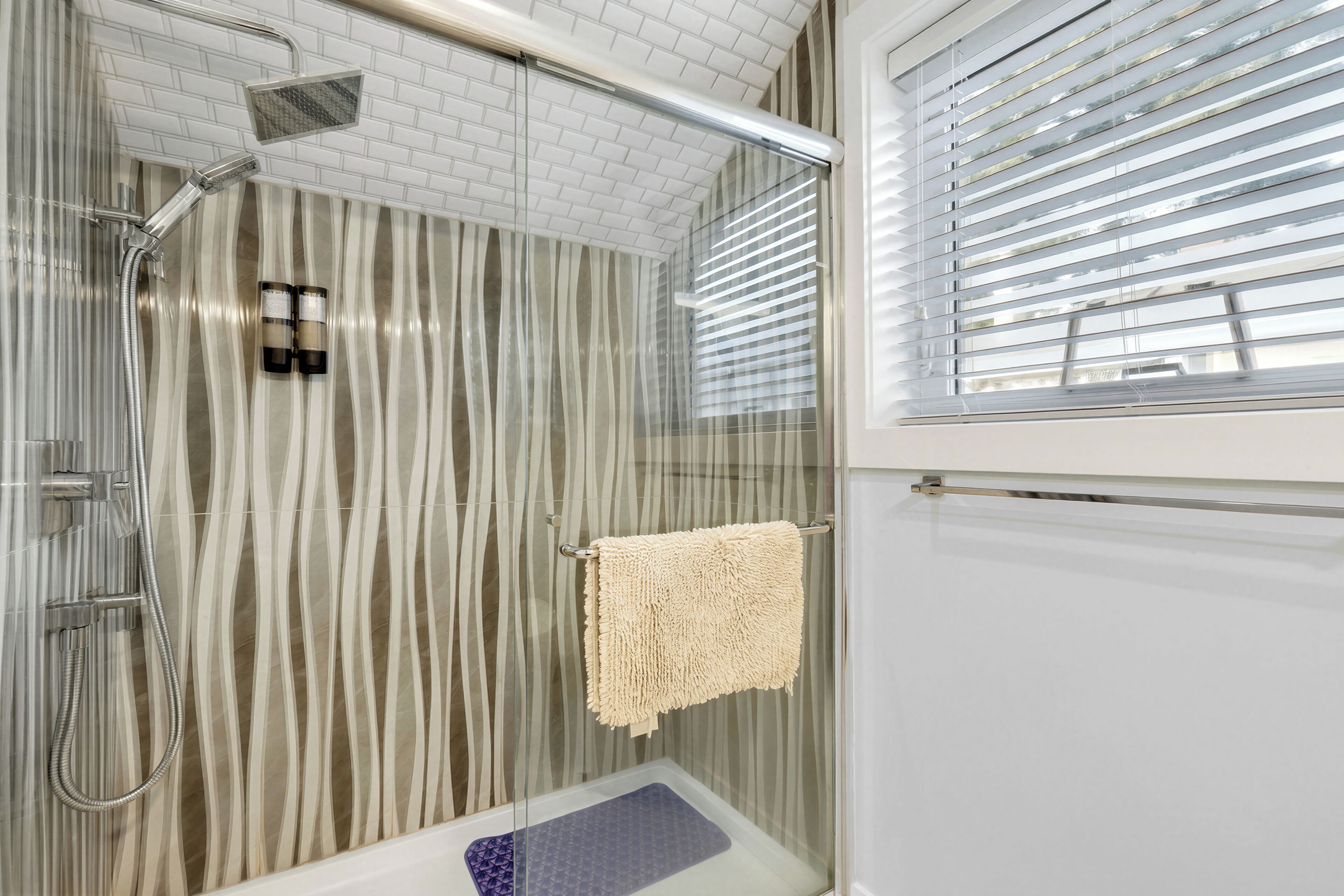 A shower with a glass door, a towel rack, and a window with blinds.
