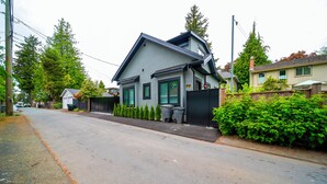 Una casa moderna de dos pisos con fachada gris y techo oscuro, ubicada en una tranquila calle residencial.