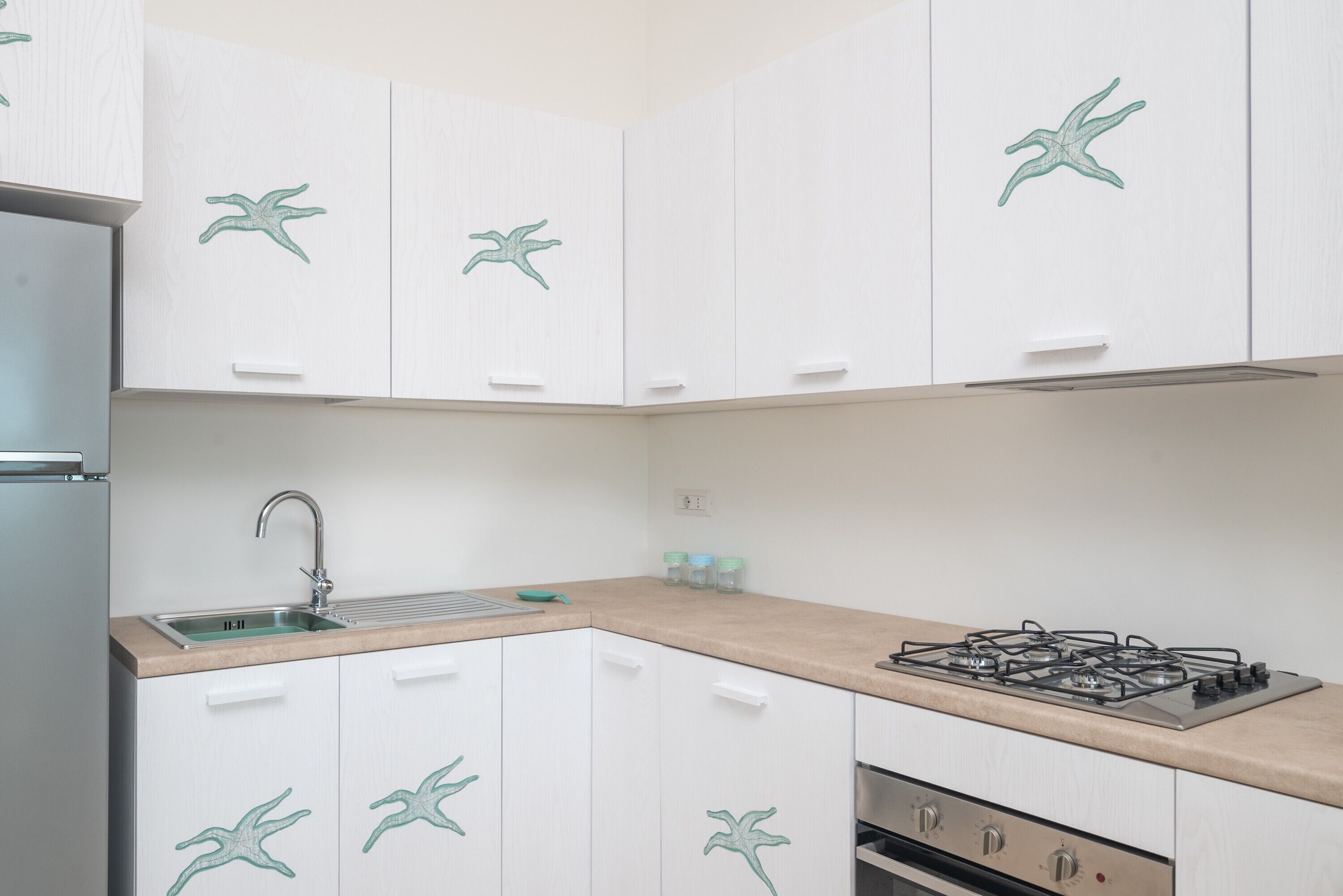 A kitchen with white cabinets, a gas stove, a sink, and a refrigerator.