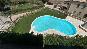 Una piscina rodeada por un césped cuidado, con vista al mar y colinas al fondo.